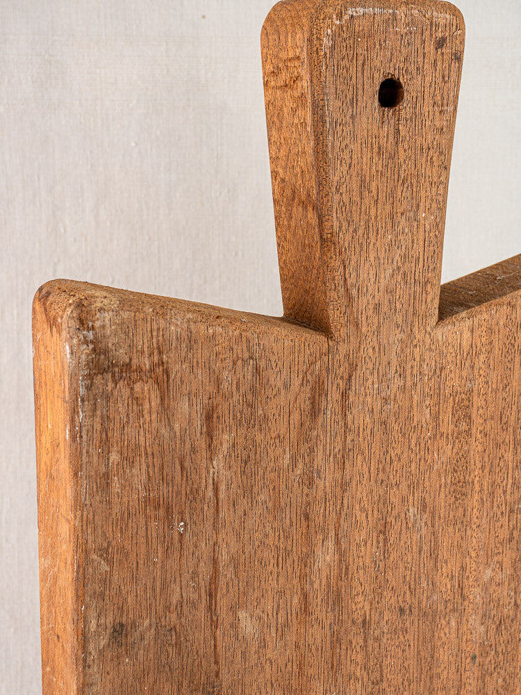 Antique French hardwood cutting board, early 20th century, with handle, hanging hole, natural brown finish, visible wood grain.