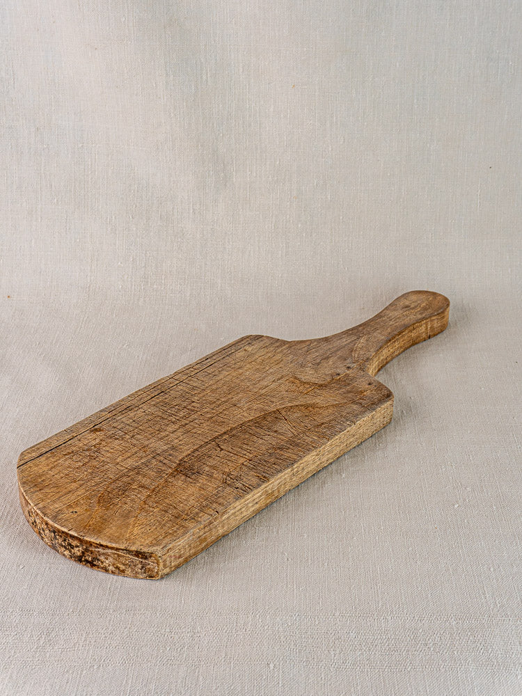 Antique French cutting board from the 1920s in oak or chestnut with aged grain, resting on light beige fabric.