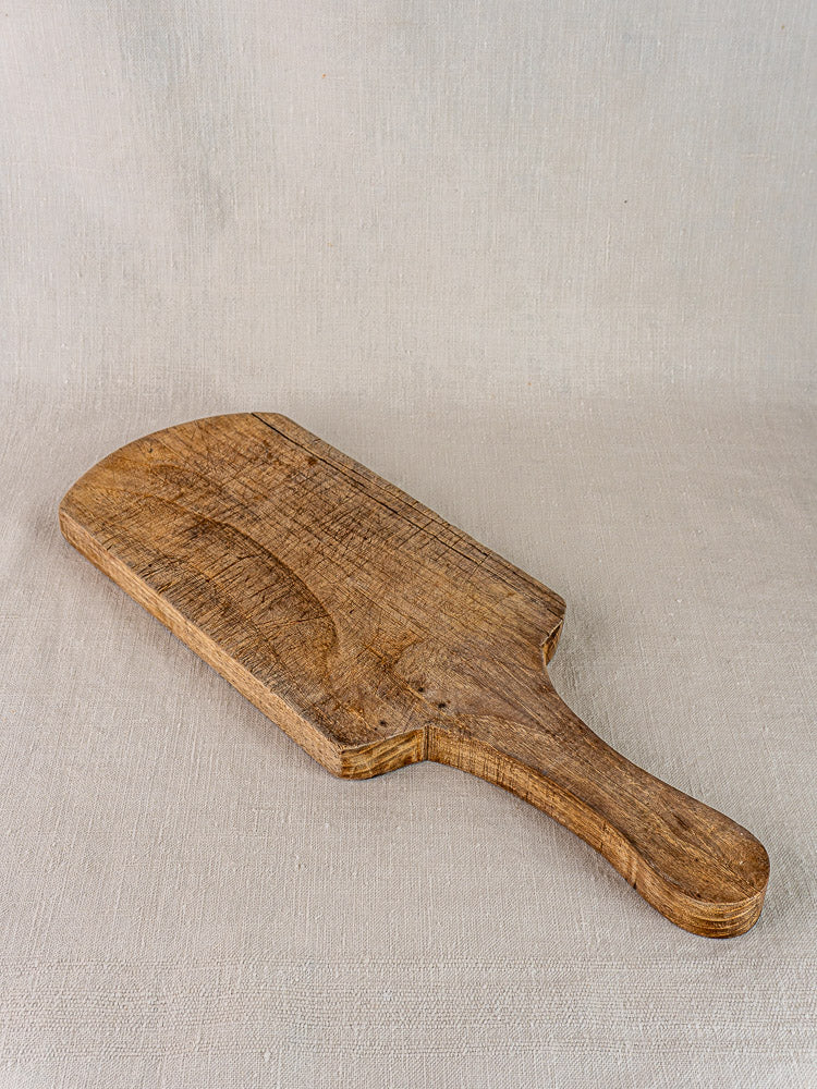 Antique French cutting board with handle, joined oak or chestnut, rustic grain, on light beige fabric.
