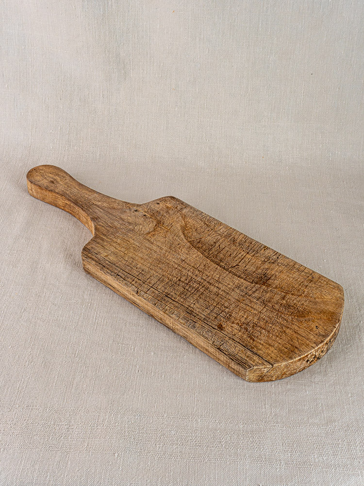 Antique French oak or chestnut cutting board with handle, 1920s, displaying rustic grain on light beige fabric.