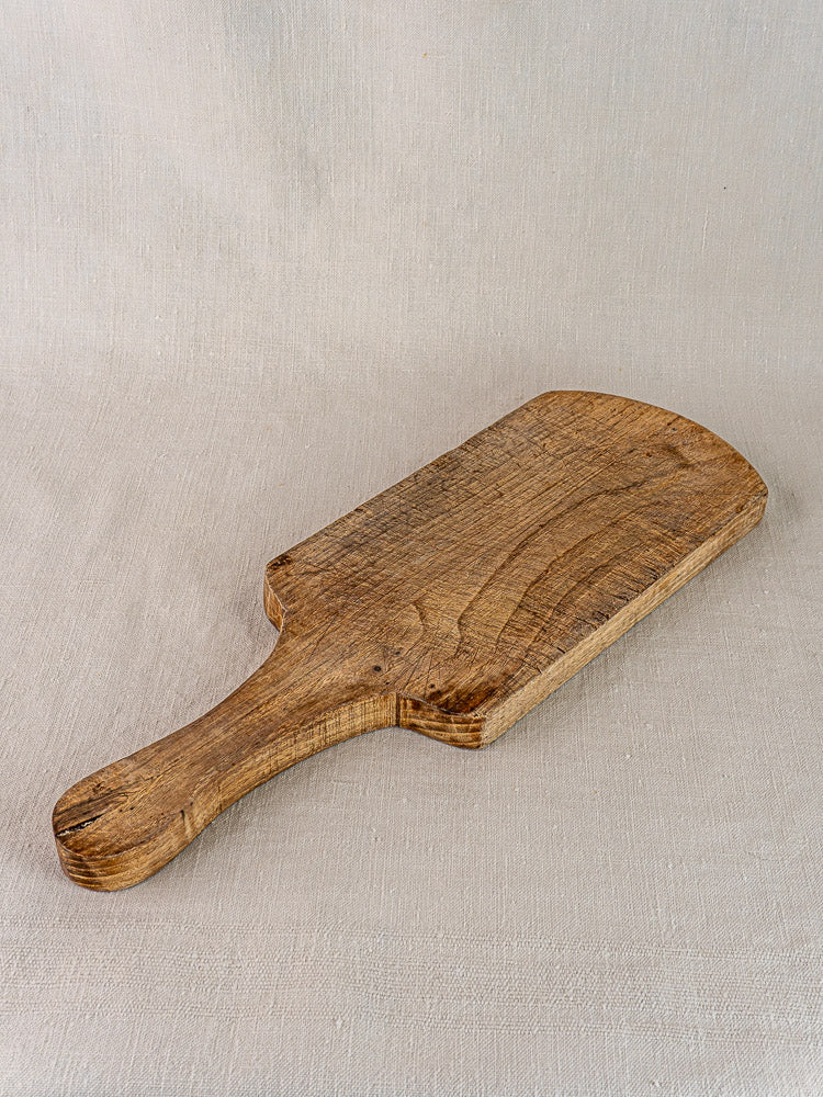 Antique French joined oak or chestnut cutting board with handle on light beige fabric. 1920s farmhouse kitchen décor.