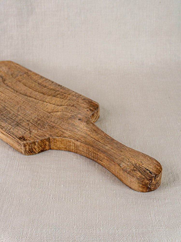Antique French cutting board in oak or chestnut with vintage patina, displayed on a light beige textured surface.