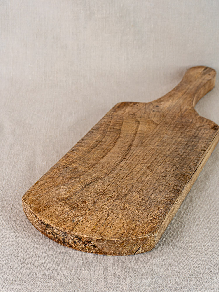 Antique French cutting board from the 1920s in oak or chestnut with visible grain atop light beige fabric.
