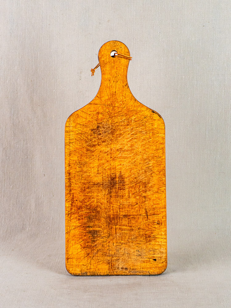 Antique French wooden cutting board with paddle handle and string, displayed upright on a plain background.