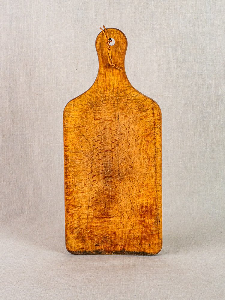 Antique French wooden cutting board with paddle handle and twine, rustic knife marks visible.