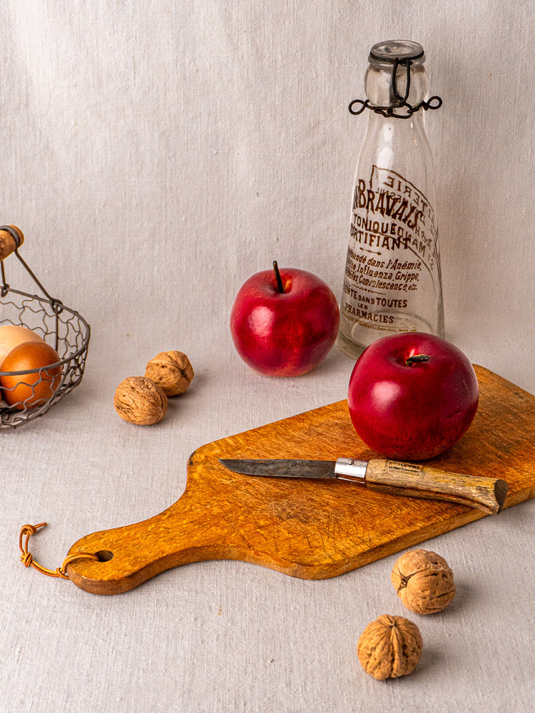 Antique French wooden cutting board with paddle handle and string, displayed upright on a plain background.