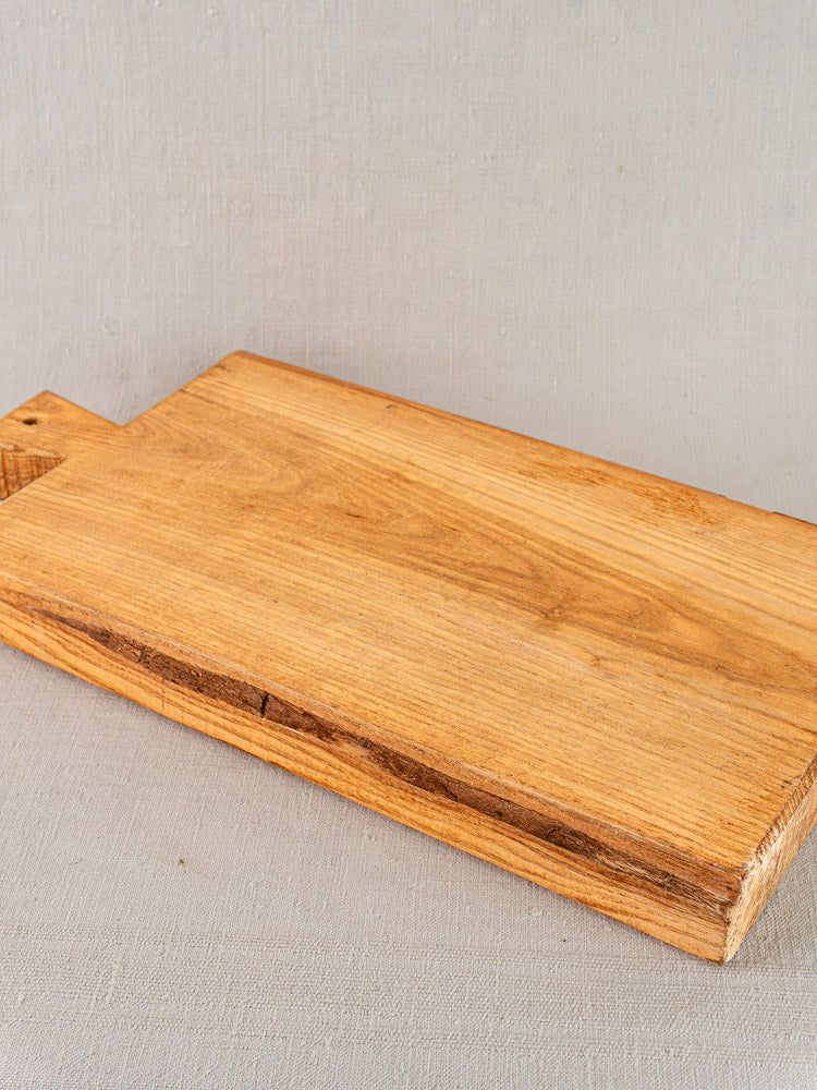 Antique French cutting board with carved paddle handle, early 20th century, natural wood grain and rough edges.