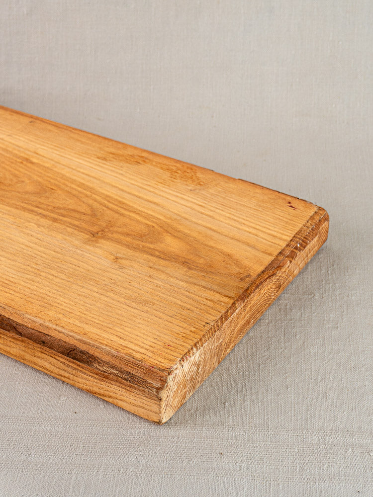 Antique French cutting board with carved paddle handle, early 20th century, on light gray textured surface.