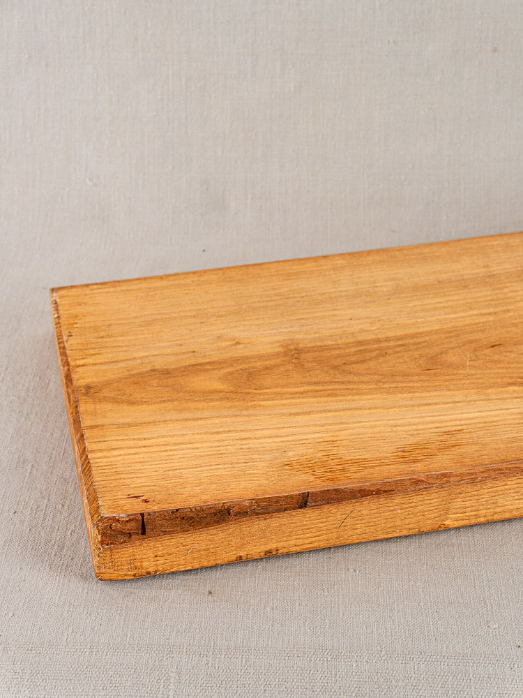 Antique French cutting board with carved paddle handle on a light gray textured surface. Early 20th century.