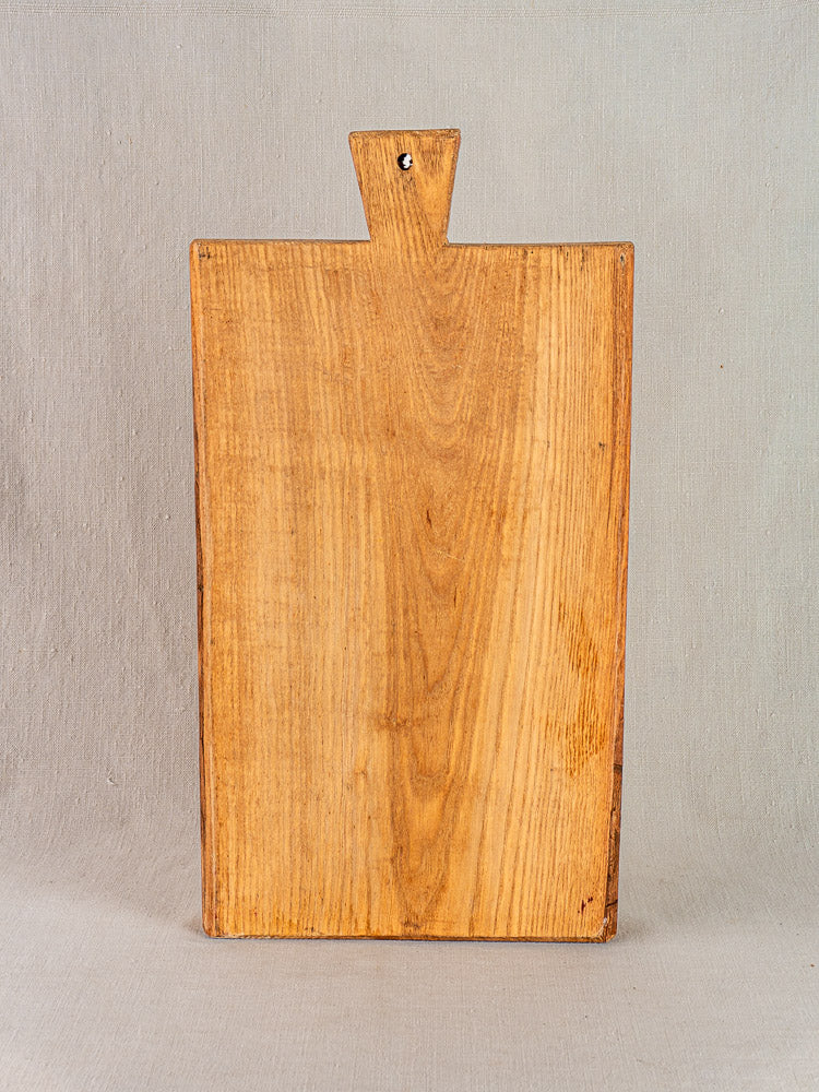 Antique French cutting board with carved paddle handle, early 20th century, displayed against light beige background.