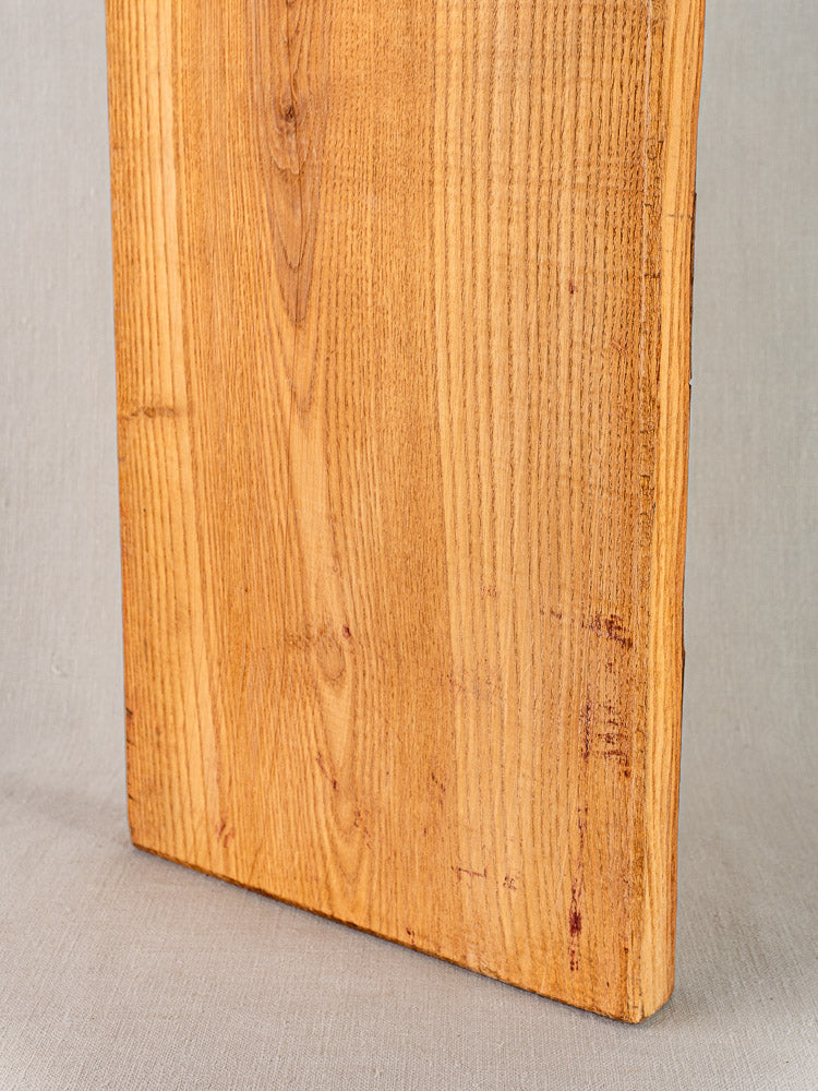 Antique French cutting board with carved paddle handle, early 20th century, upright on light gray surface showing wood grain.