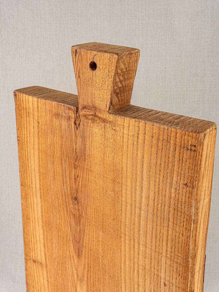 Antique French cutting board with carved paddle handle and hanging hole, early 20th century, on light background.