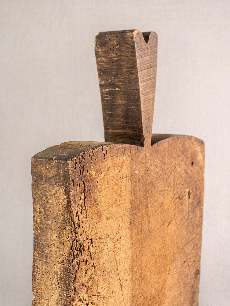 Antique French cutting board with thick handle, carved notch, and weathered grain on a neutral gray background.