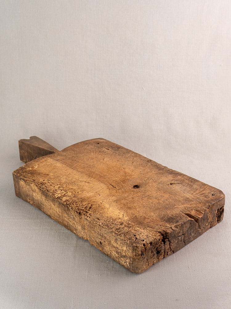 Antique French cutting board from the 1880s with worn surface and handle, displayed on a light background.