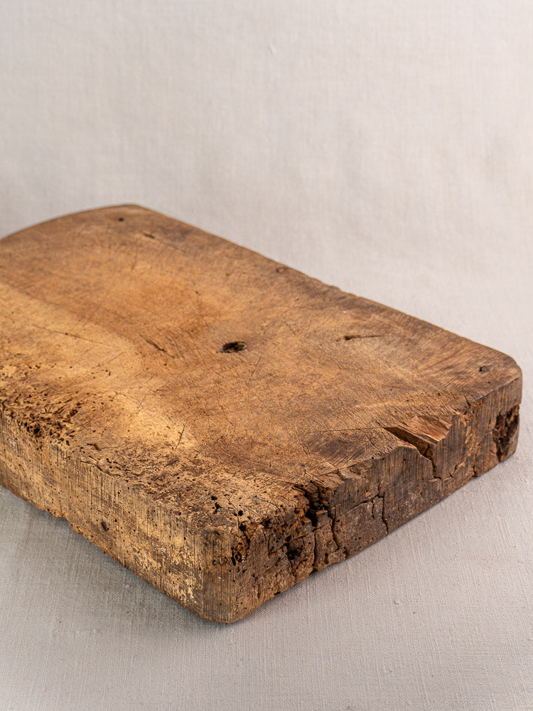 Antique French cutting board with rustic texture and cracks displayed on light gray fabric background.