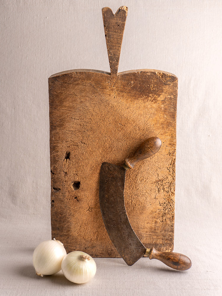 Antique French cutting board with rough texture and heart-shaped handle, upright against a light gray background.