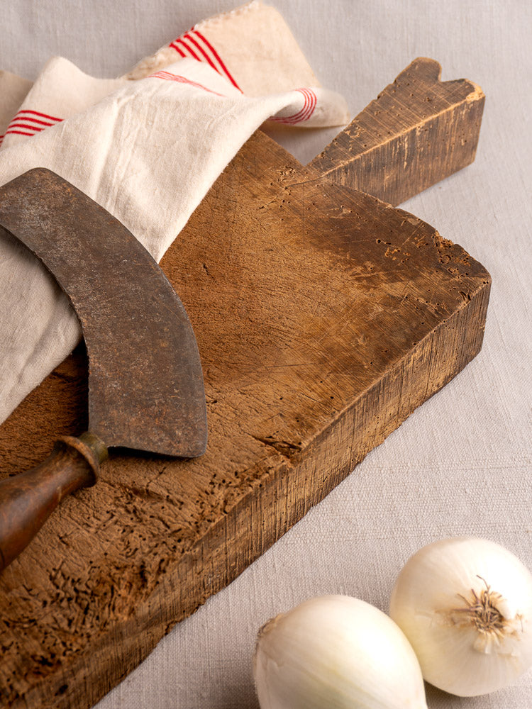 Antique French cutting board circa 1880s with vintage knife, striped cloth, and white onions on neutral fabric.