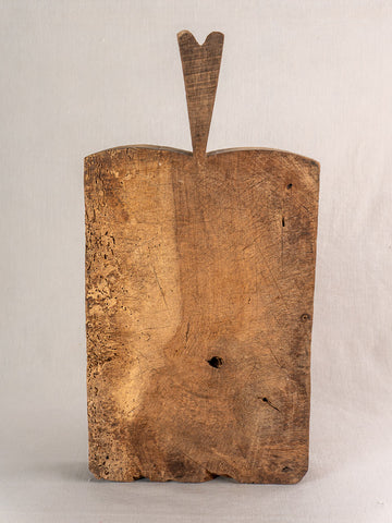 Antique French cutting board with rough texture and heart-shaped handle, upright against a light gray background.