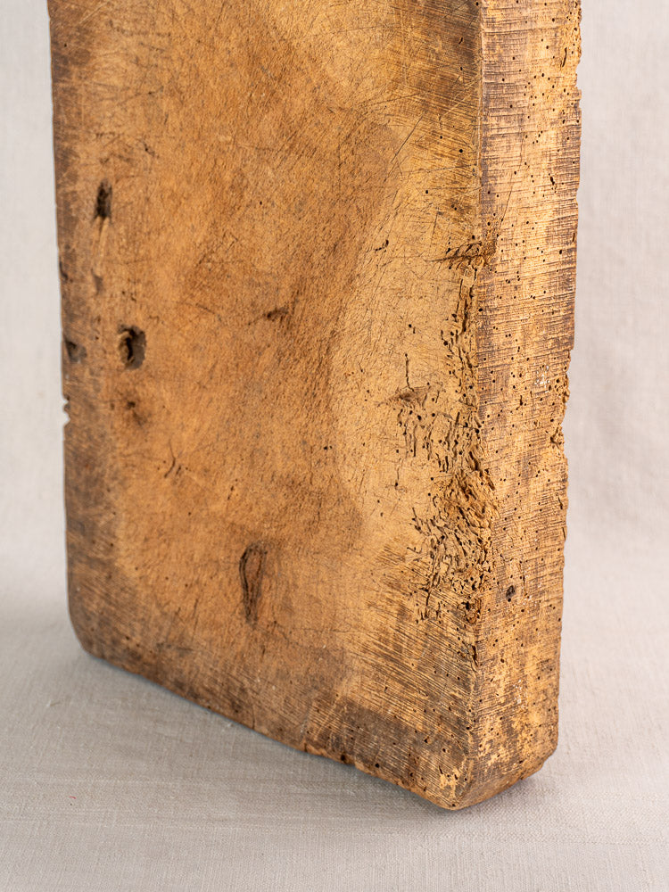 Antique French cutting board, circa 1880s, thick weathered wood with rough edges, on light fabric background.