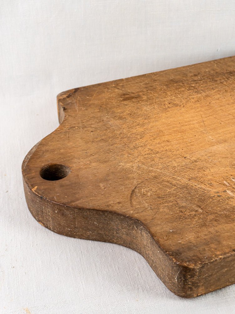 French antique beech chopping board c. 1900 with corner hole on light fabric surface.