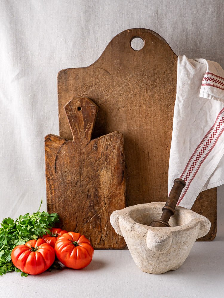 French antique beech chopping board with rustic wood board, white mortar and pestle, tomatoes, parsley, and striped cloth.