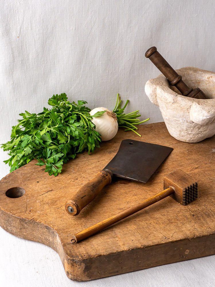 Antique French beech chopping board with parsley, onion, cleaver, tenderizer, and marble mortar and pestle.