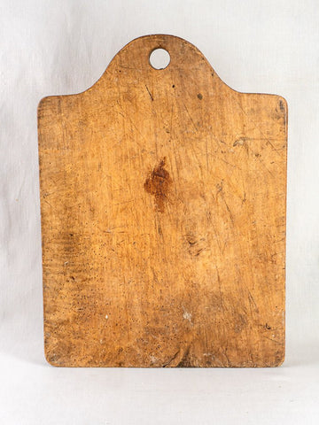 Antique circa 1900 French beech chopping board with rounded top and central hole, upright on light background.