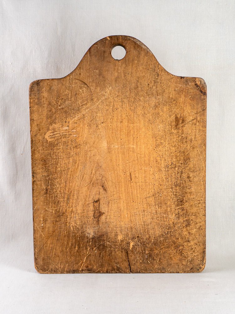 Antique French beech chopping board, c. 1900, with rounded top and hanging hole on plain background.