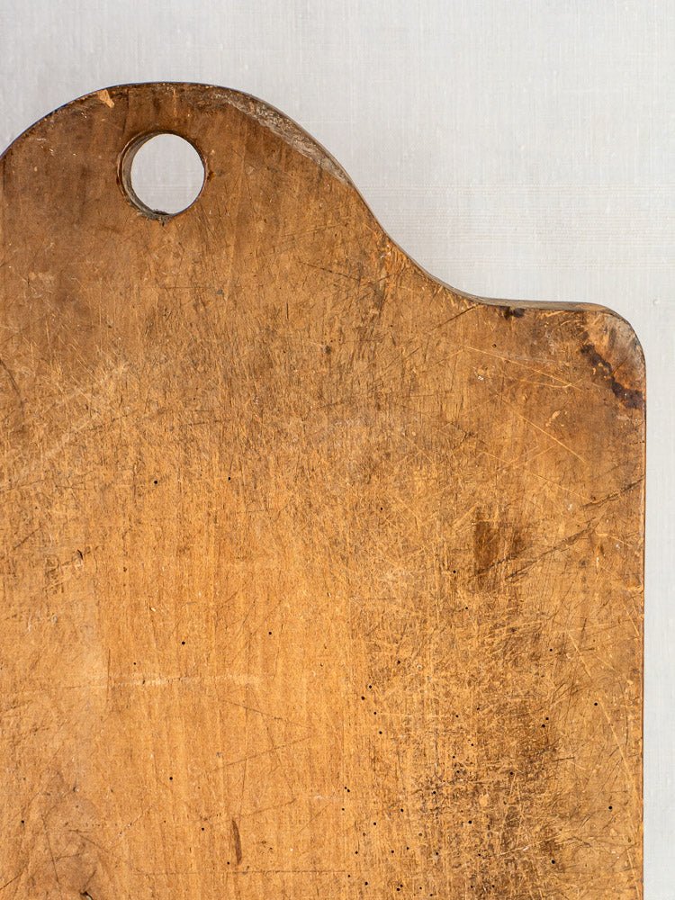 Antique French beech chopping board circa 1900 with rounded top and hanging hole on light background.