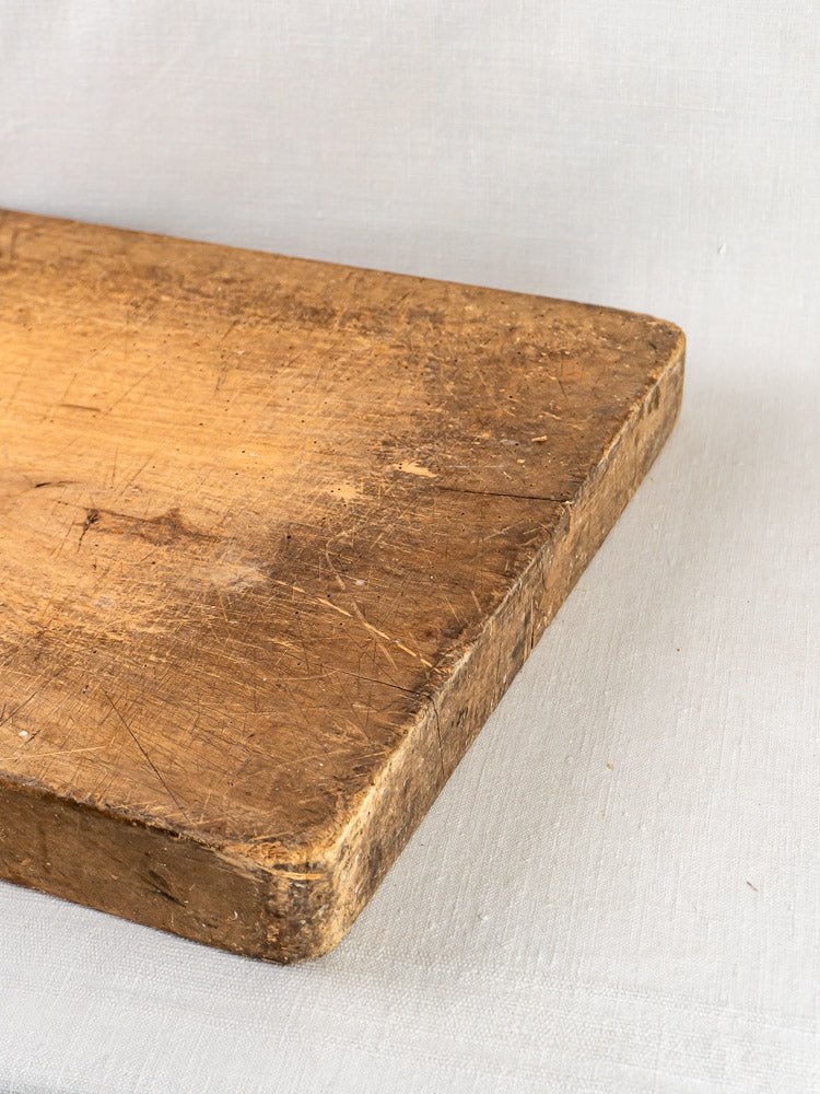 Antique French beech chopping board c. 1900 with timeworn surface atop light fabric.