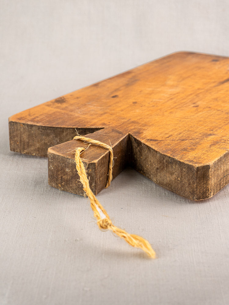 Antique French cutting board, late 19th century, single plank with rustic edge and twine loop on gray surface.
