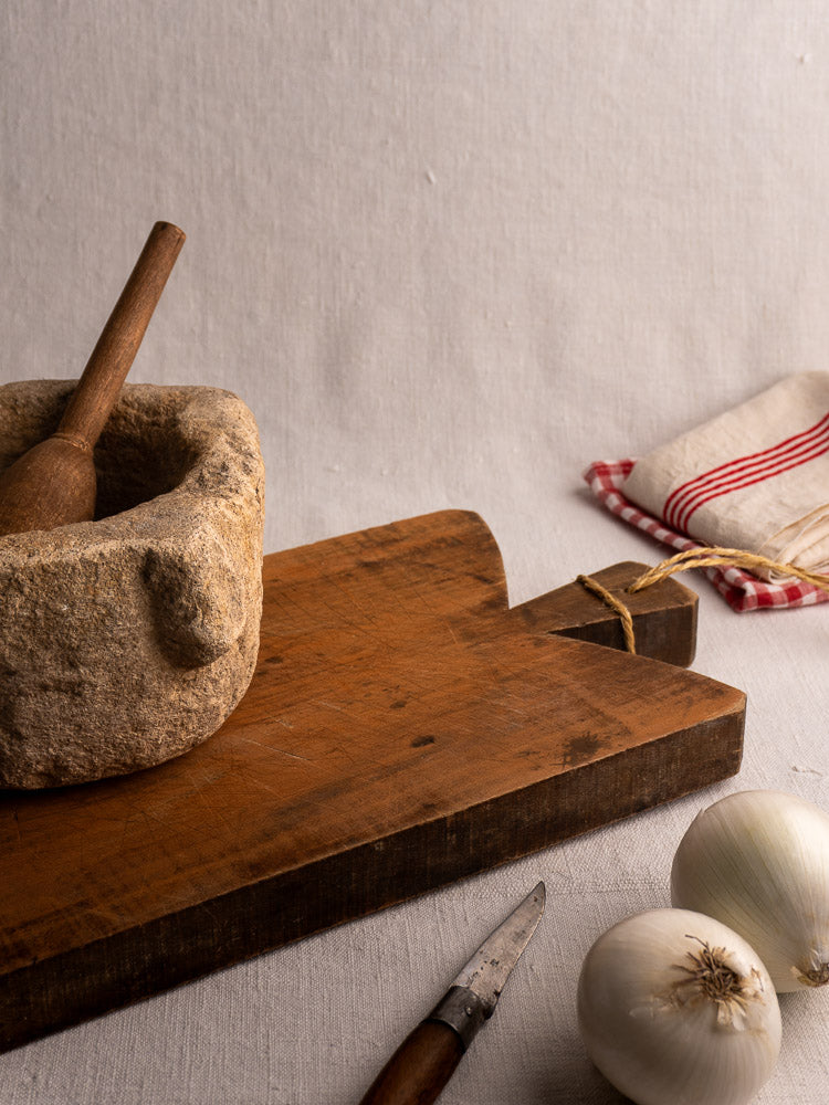 Antique French cutting board with handle and twine, single plank, upright against a light gray background.