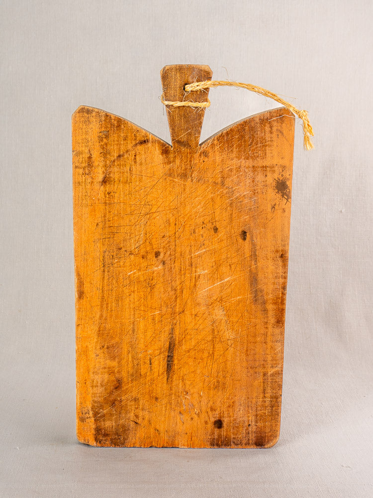 Antique French cutting board with handle and twine, single plank, upright against a light gray background.