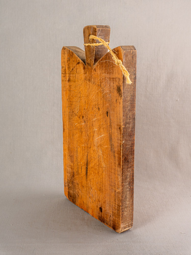 Late 19th-century French antique cutting board with knife marks, short handle, and rope loop displayed upright.