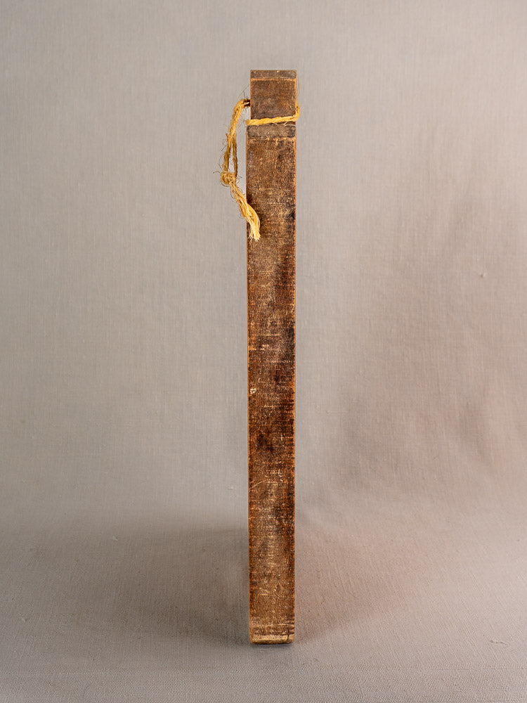 Antique French single-plank cutting board with frayed yellow string, upright on a beige background.