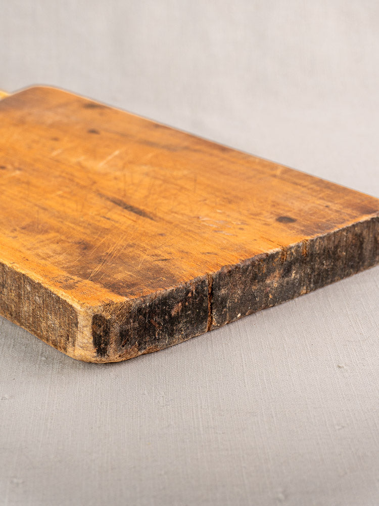 Antique French cutting board, single plank with knife marks and darkened edge on a light grey surface.