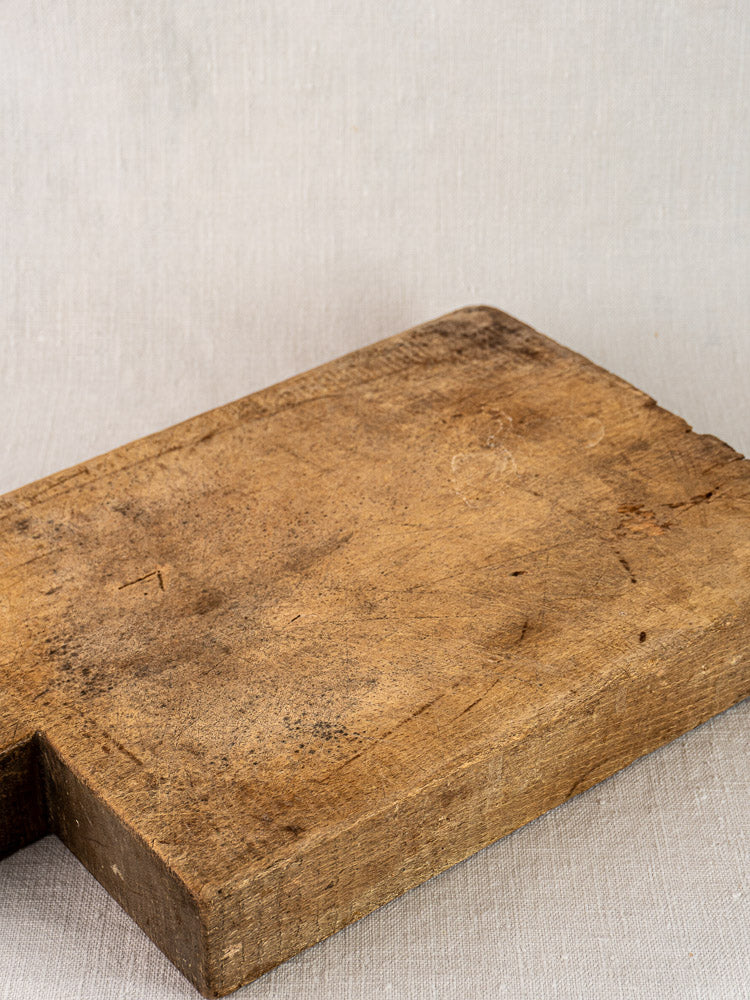 Antique French cutting board circa 1900 with tongue handle on a light neutral fabric background.