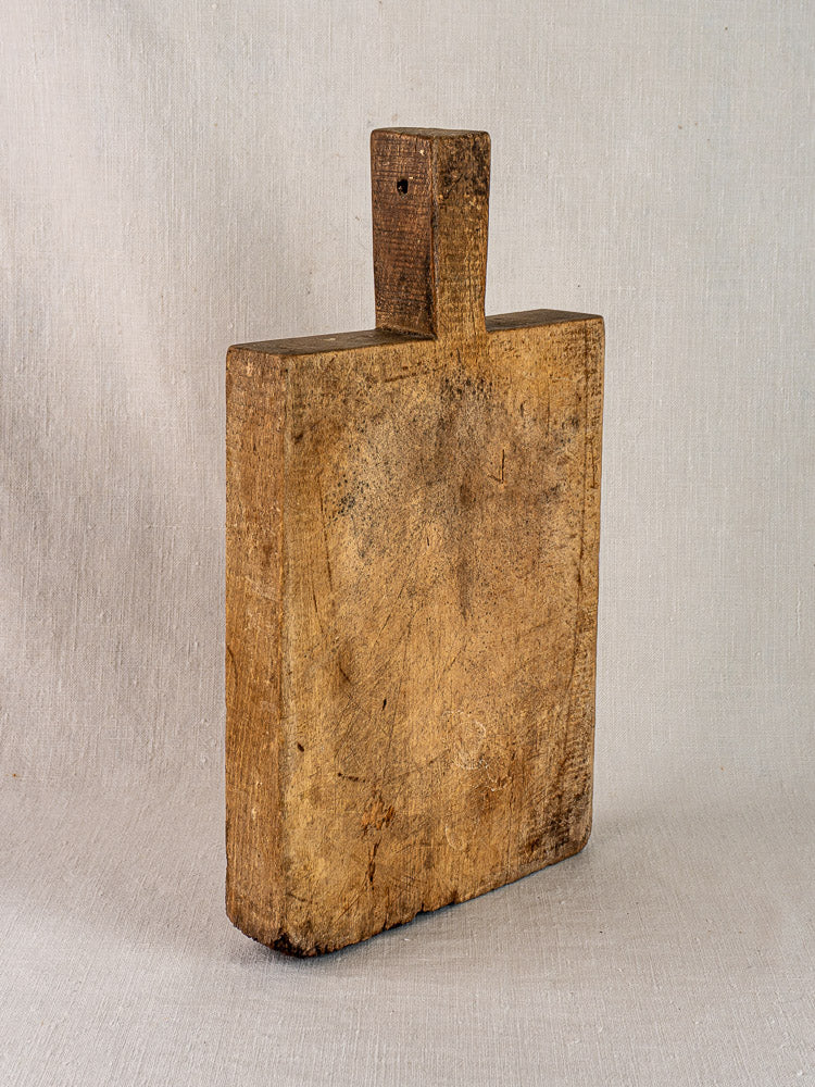 Antique French cutting board with tongue handle from circa 1900 displayed upright on neutral fabric.