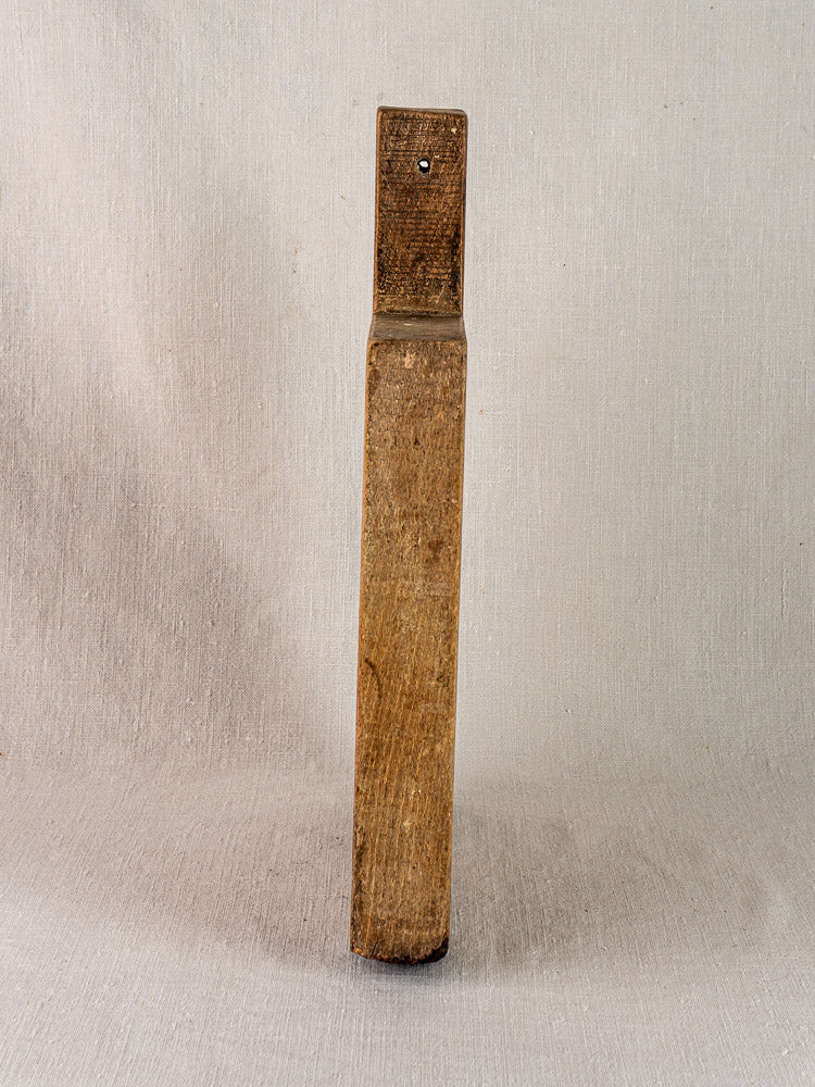 Antique French cutting board, circa 1900, solid wood with tongue handle and hole, upright on neutral fabric.