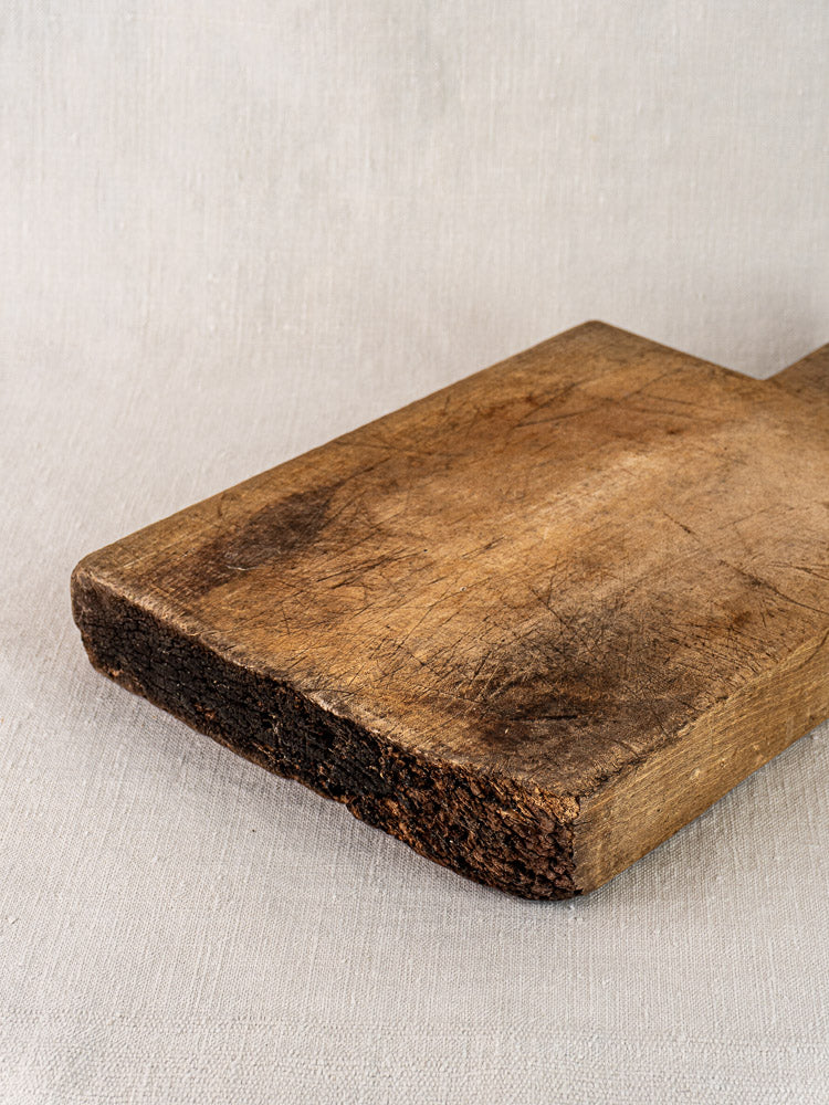 Antique French cutting board with tongue handle, visible scratches, and darkened edge on light textured fabric. Circa 1900.