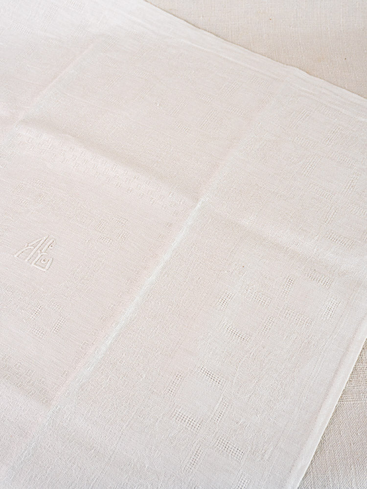Set of 12 antique French damask linen napkins with delicate white texture and subtle AB monogram, displayed on a light surface.