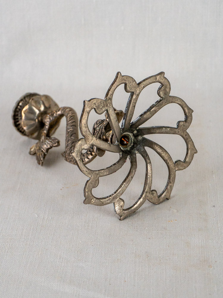 Antique French silvered metal Dolphin Candlesticks with ornate floral cutouts and twisted stems on light fabric.