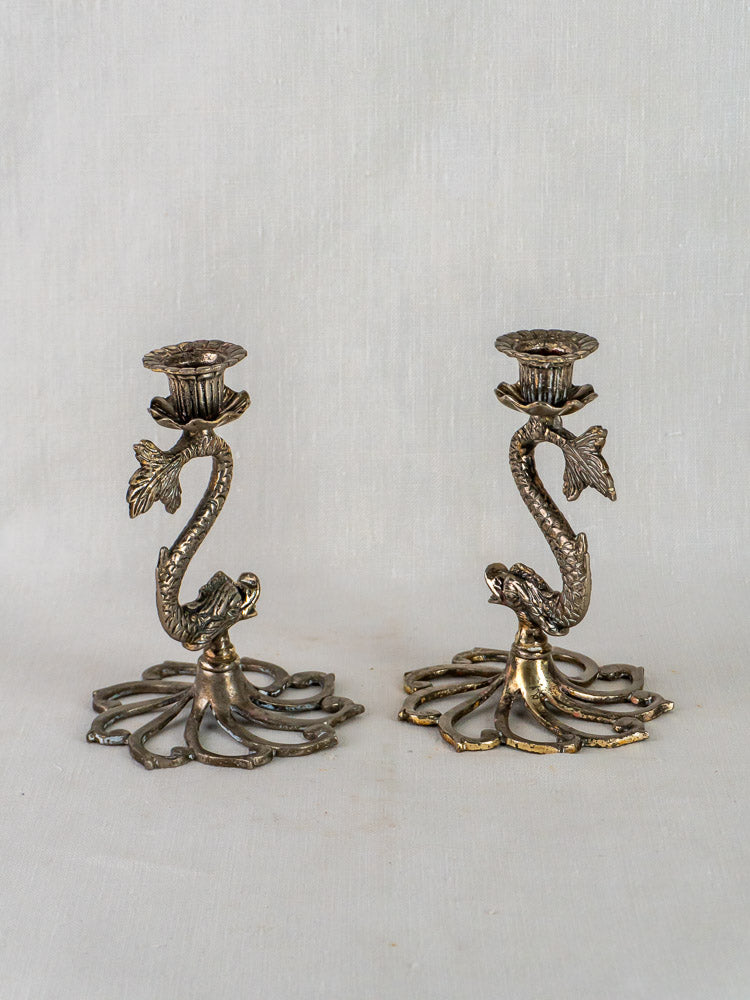 Pair of antique French silvered metal dolphin candlesticks with sculptural details on neutral background.