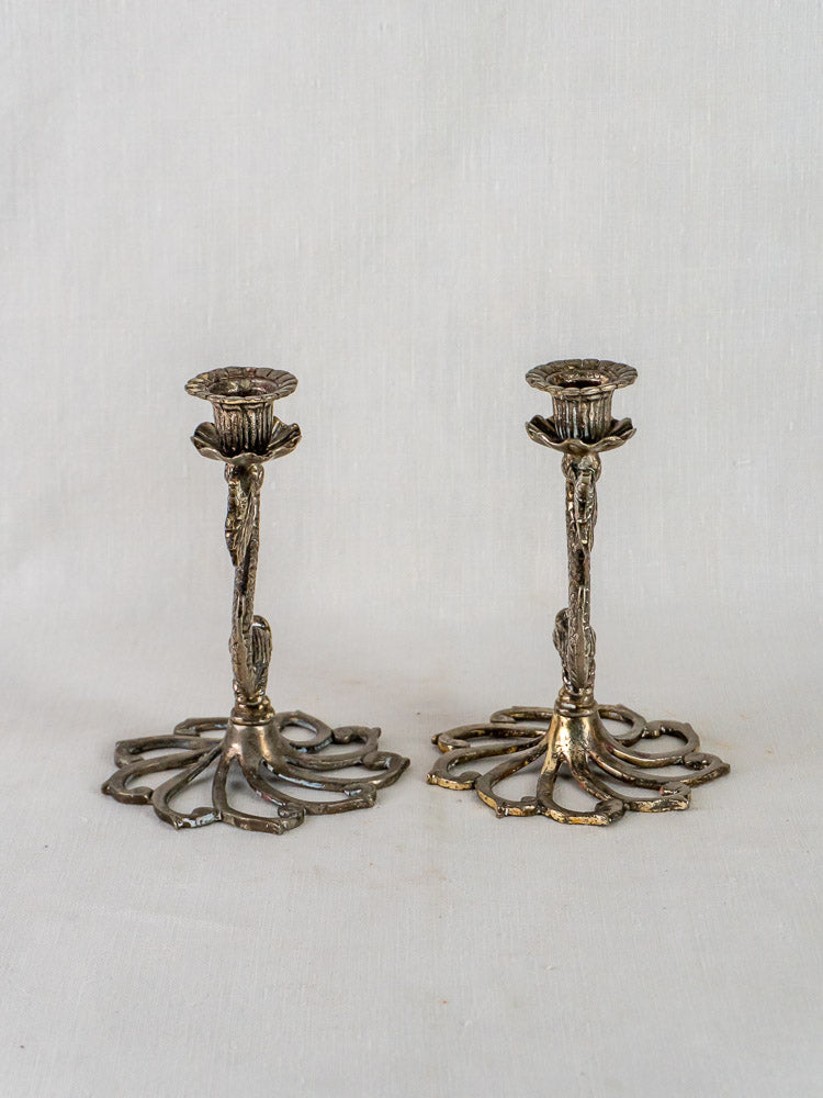 Pair of French Dolphin Candlesticks in antique silvered metal on white fabric background.