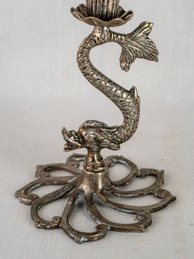 Pair of antique French silvered metal dolphin candlesticks with curling tails on a plain background.