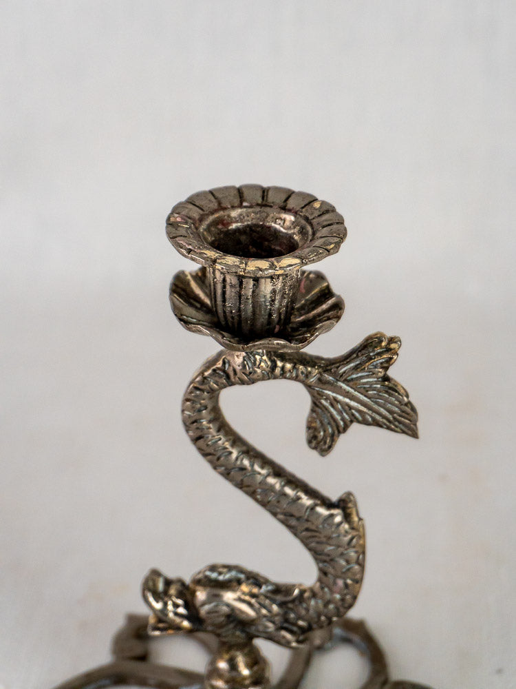 Antique silvered metal candlesticks with sculptural fish forms, detailed scales, curling tails, on decorative bases.