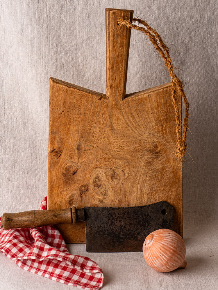Antique French elm cutting board with rope handle, mid 19th century, vintage cleaver, checkered cloth, and onion.