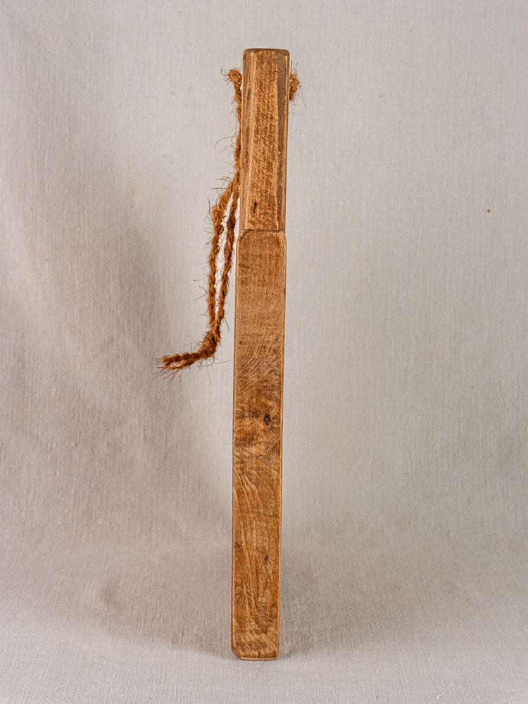 Antique French elm cutting board with rope handle, rustic mid-19th century texture, set against neutral fabric.