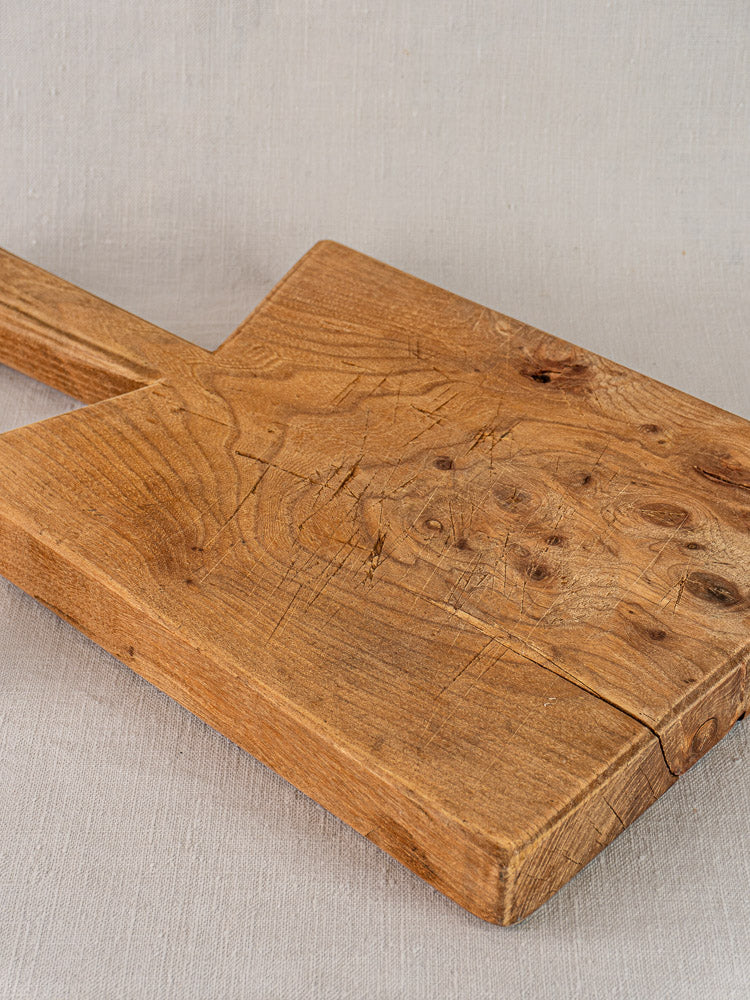 Antique French elm cutting board with rope handle, mid 19th century, showing visible grain on light gray fabric.