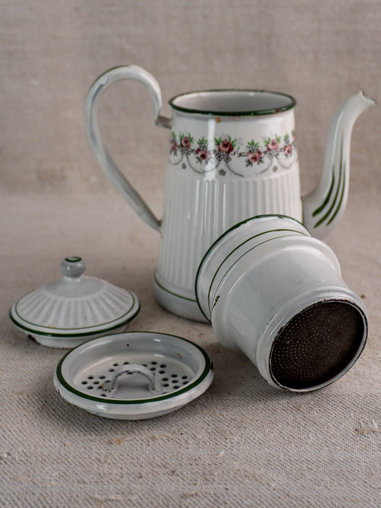 Antique French enamel coffee pot by B.B. Frères, white floral design, green accents, disassembled on beige fabric.